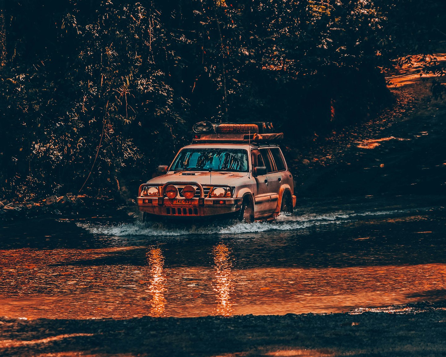 Off-road SUV driving through a shallow forest stream.
