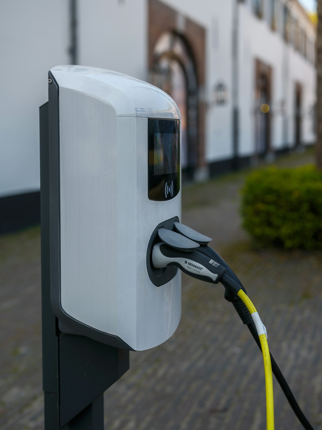 Electric vehicle charging station plugged into a car on pavement.