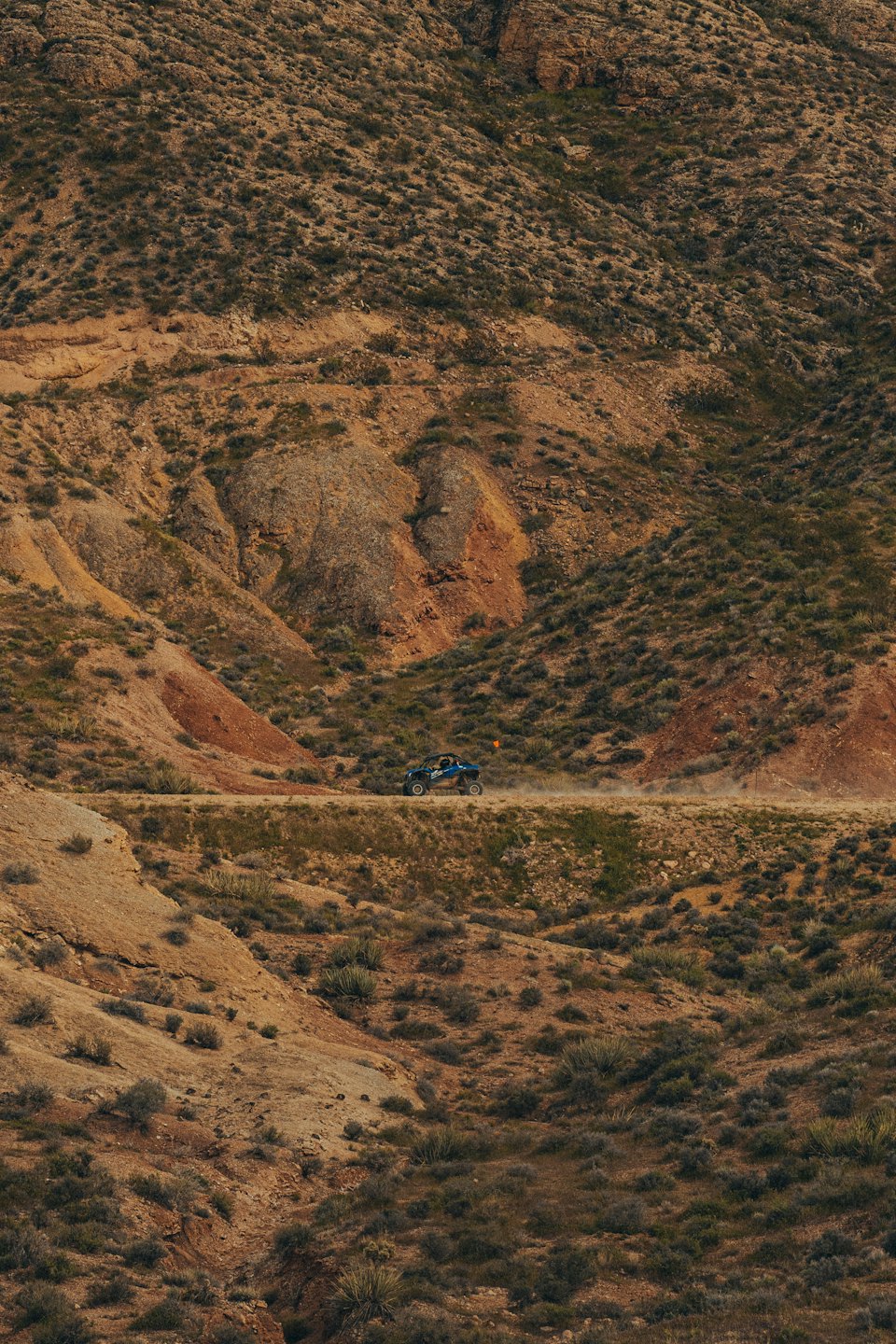 Blue off-road vehicle drives along a dusty desert dirt track.