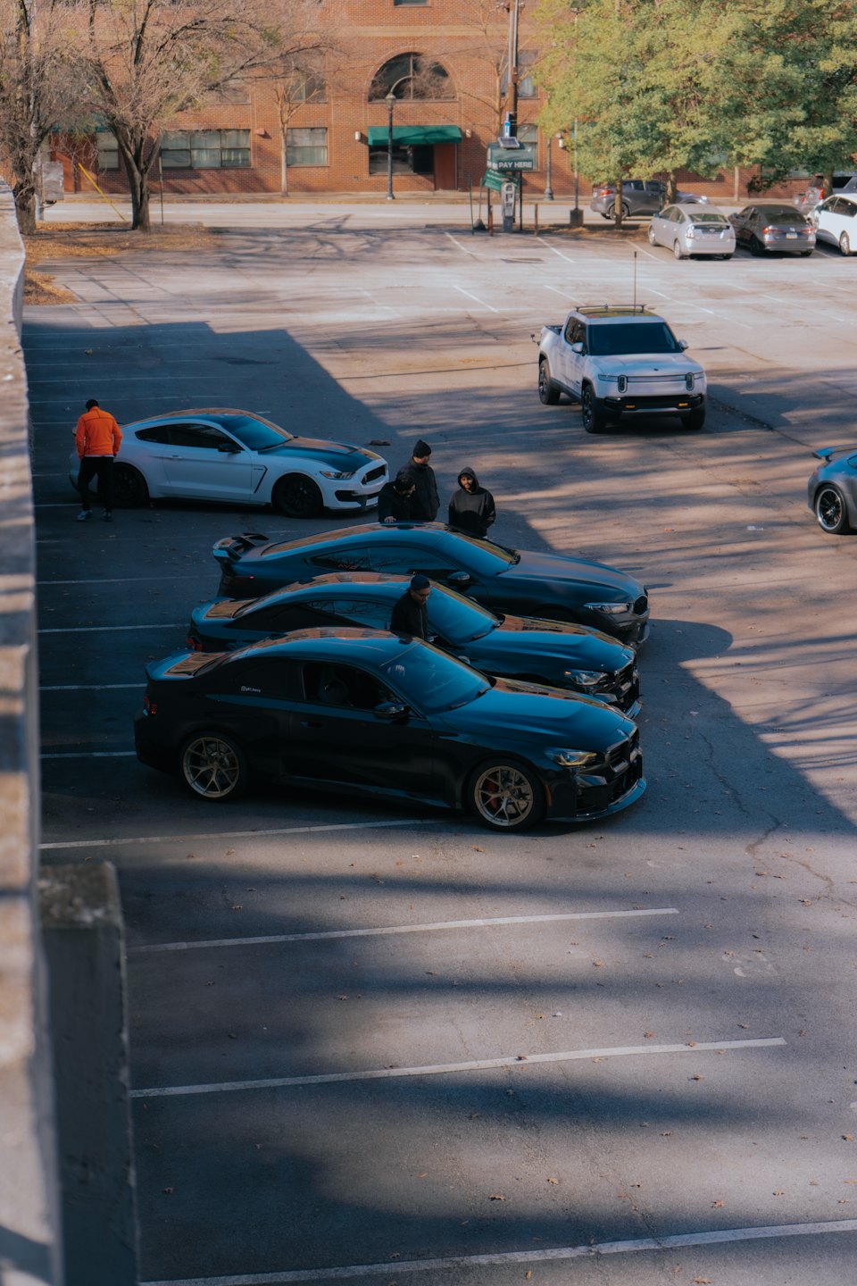 Young men with performance cars and electric truck in parking lot.