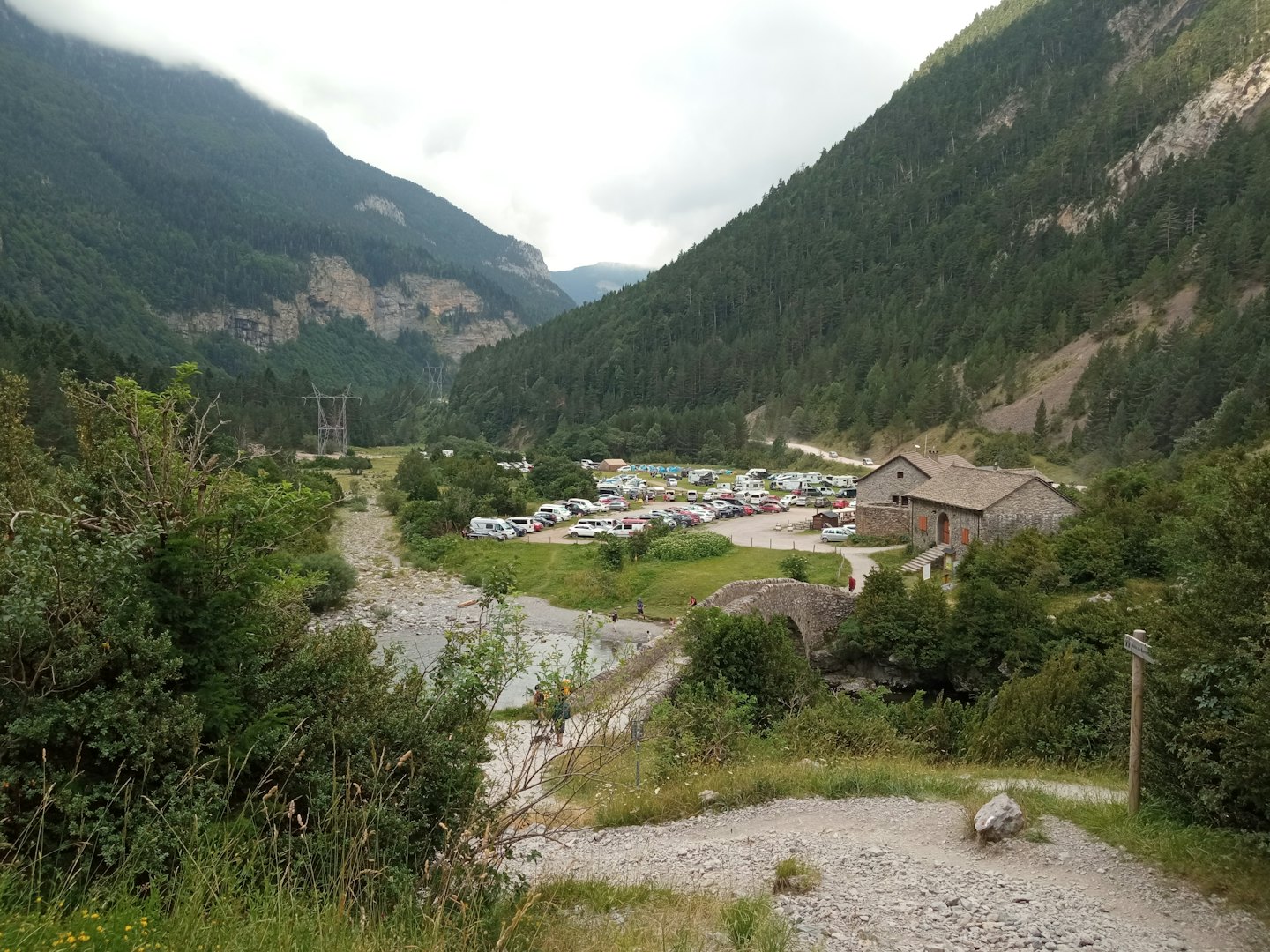 Cars parked near a stone building and bridge in a valley.