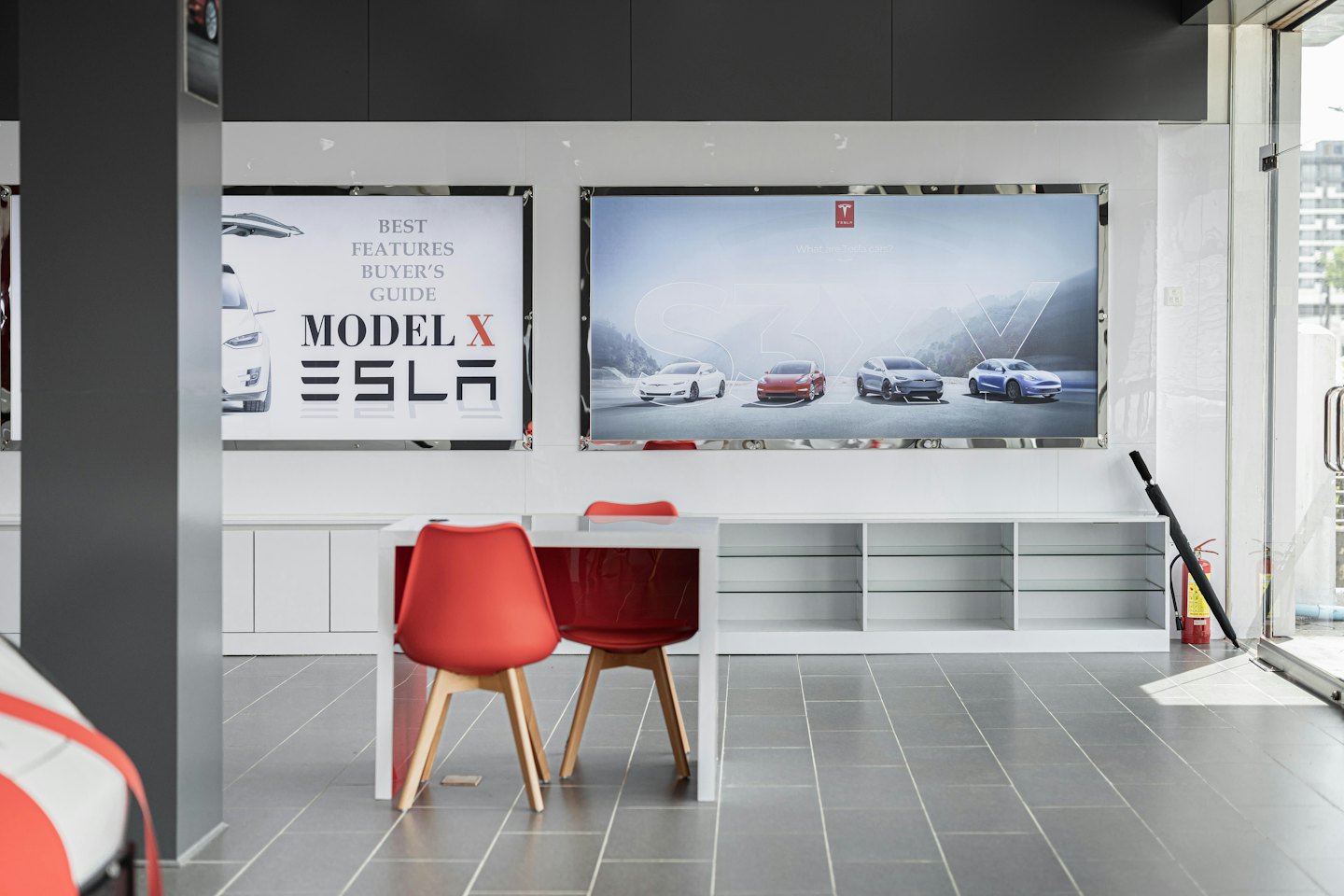 Modern electric car showroom with red chairs and promotional posters.