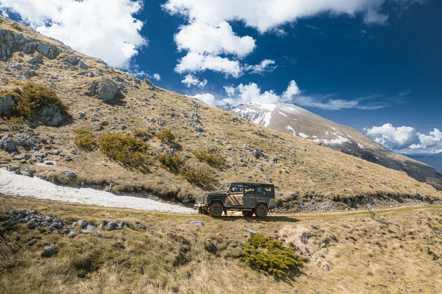 An off-road vehicle driving along a winding mountain dirt path.