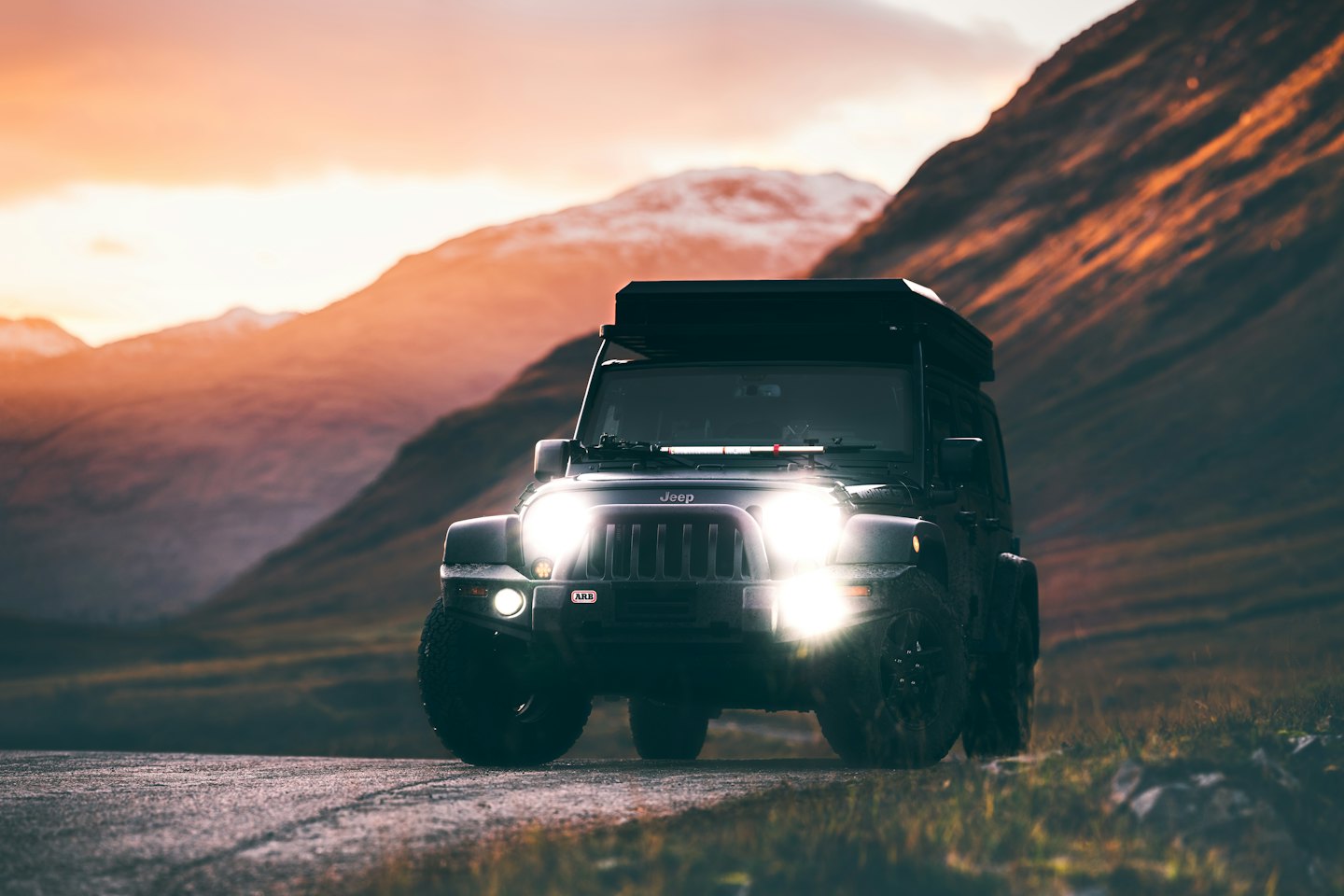 Off-road SUV with roof tent driving on mountain road.